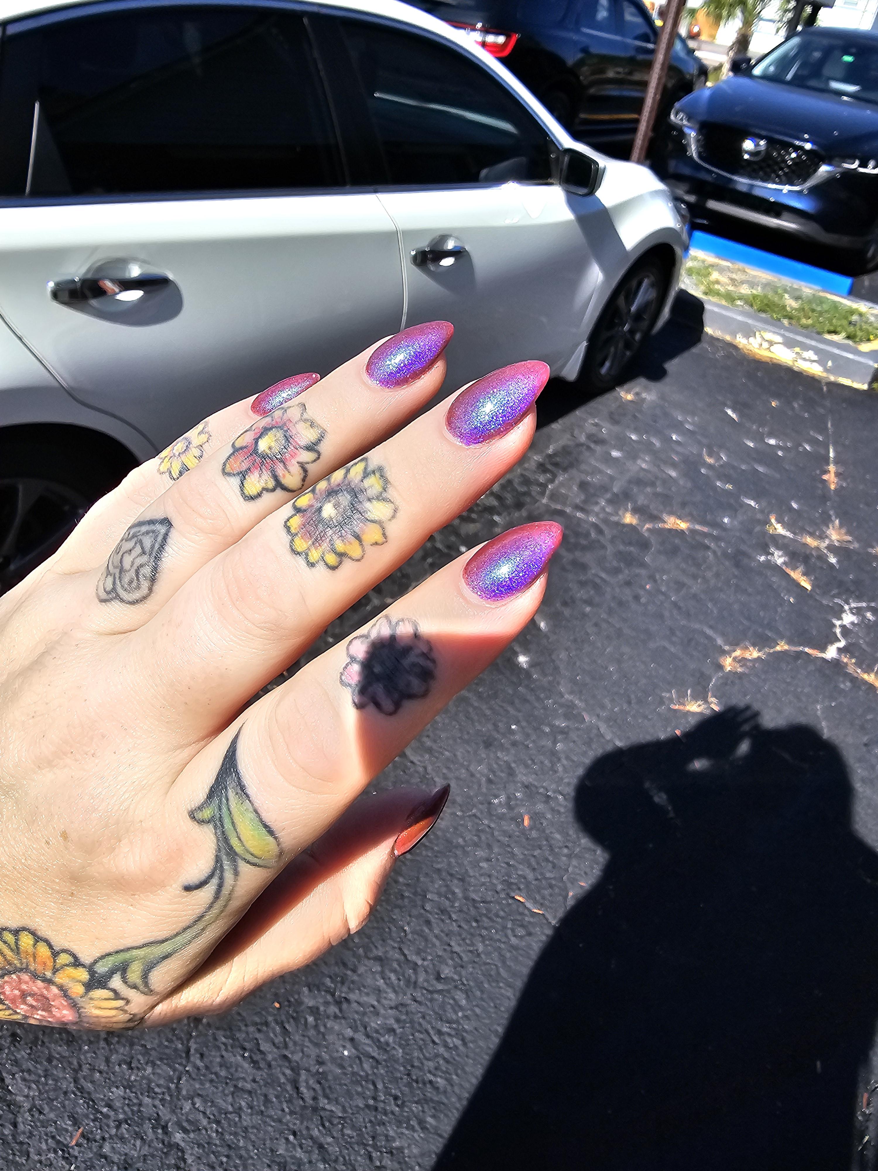 Hand with purple metallic nail polish and floral tattoos posed against a black BMW car