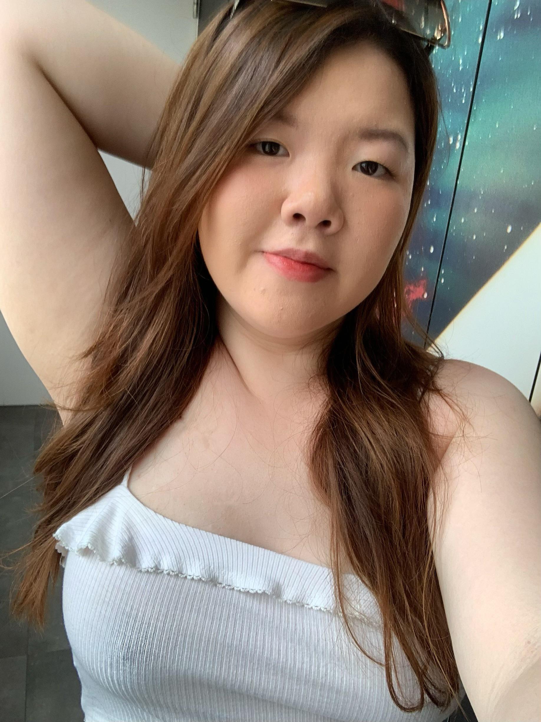 Curvy Asian woman posing braless in a white ribbed crop top and blue jeans
