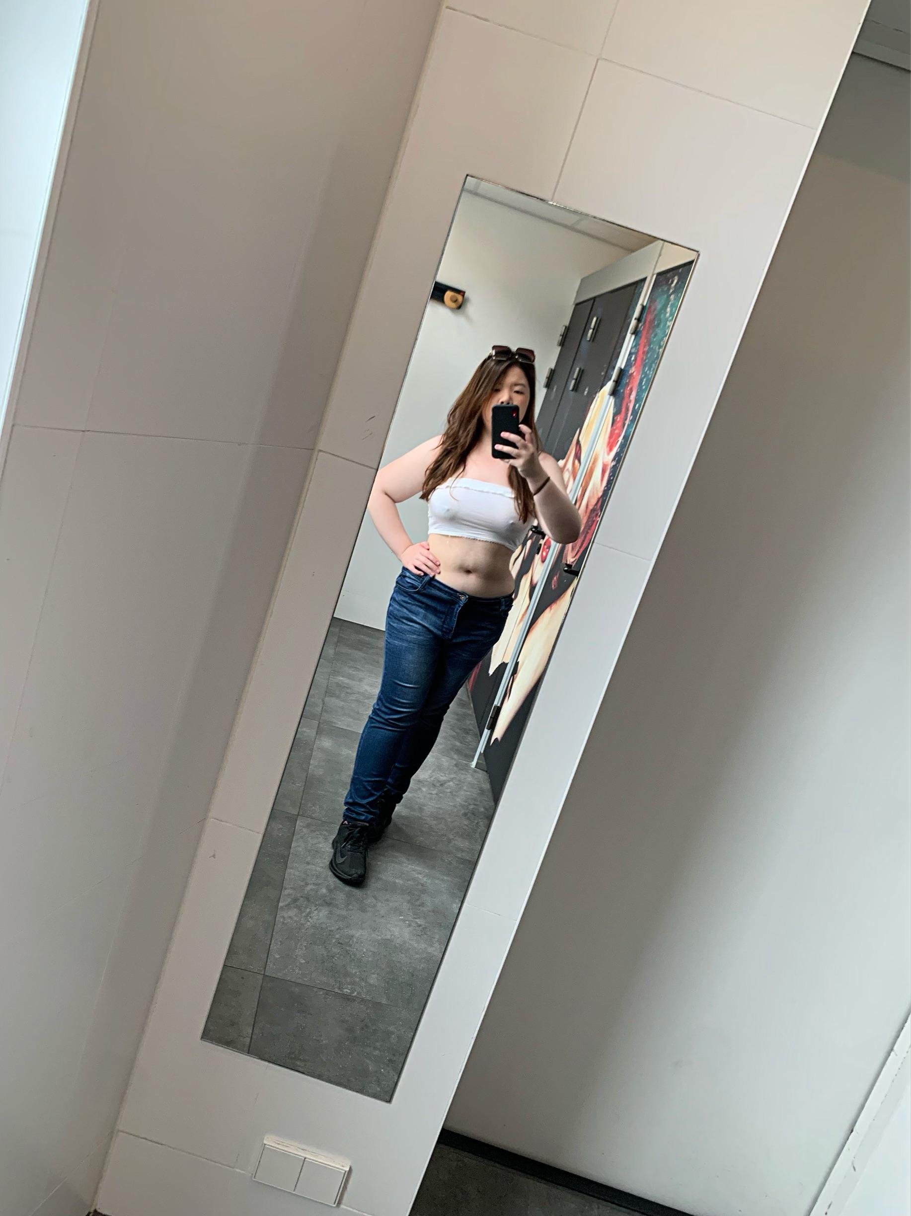 Curvy Asian woman posing braless in a white ribbed crop top and blue jeans