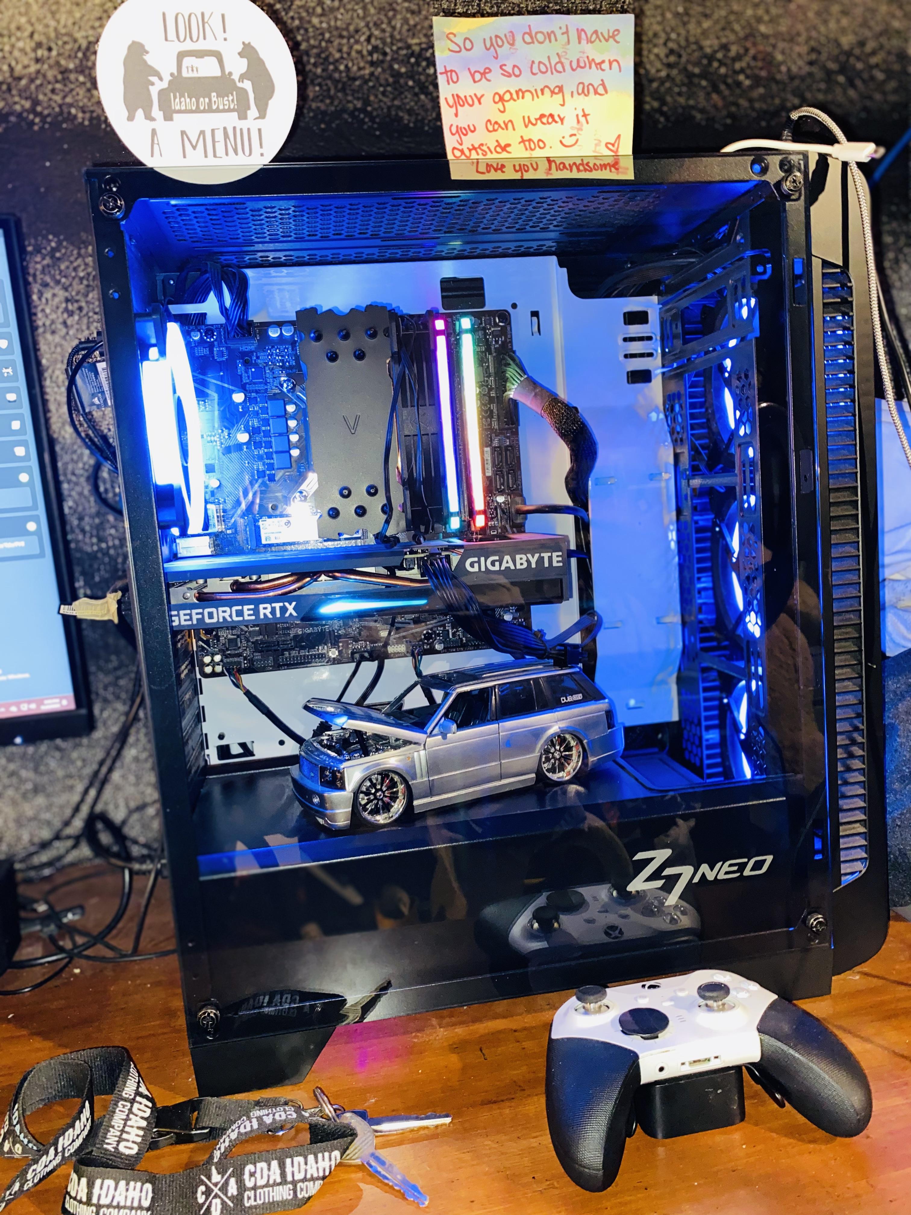 Custom gaming PC build with blue lighting and a small silver model car inside the case on a wooden desk