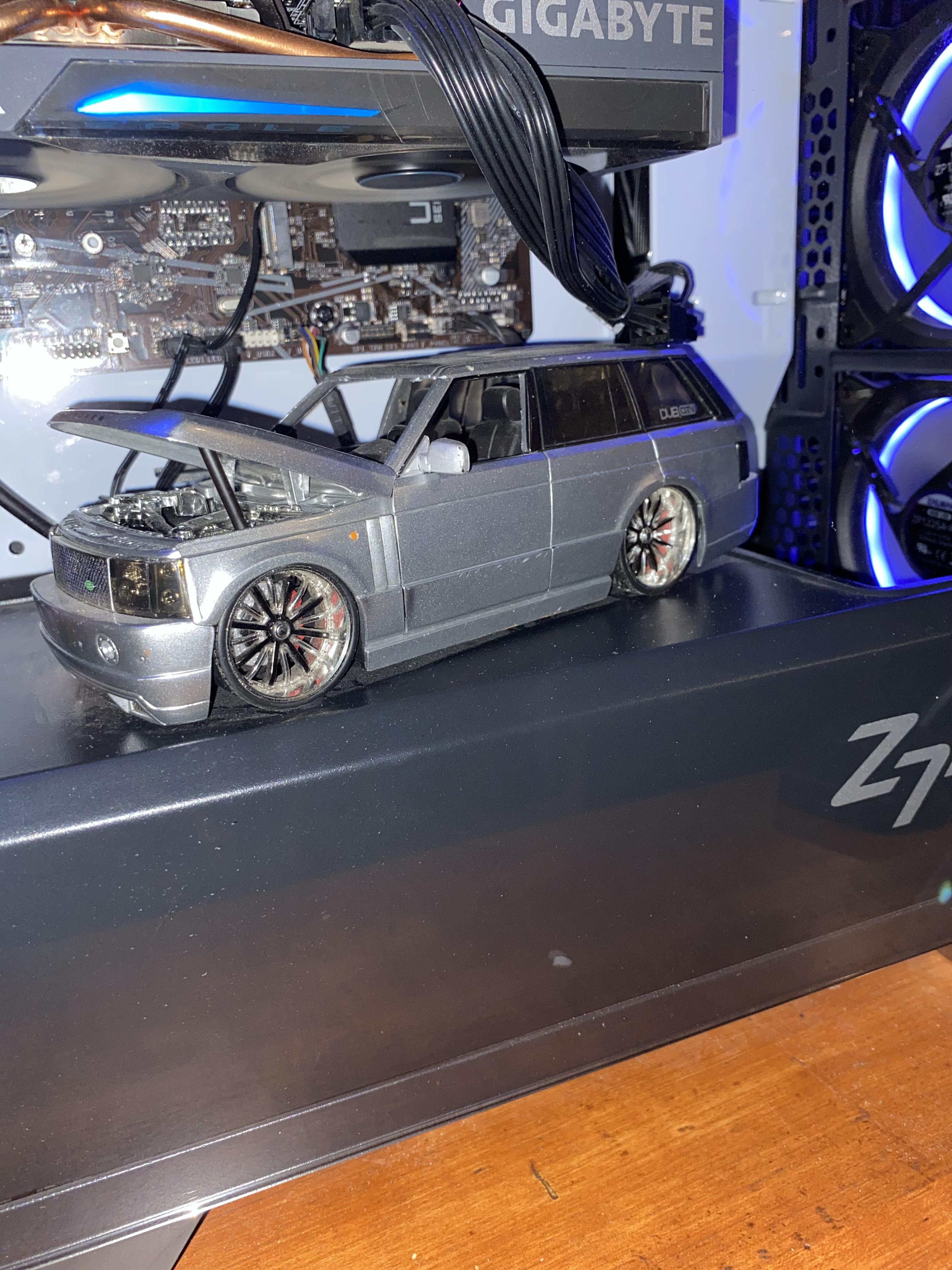 Custom gaming PC build with blue lighting and a small silver model car inside the case on a wooden desk