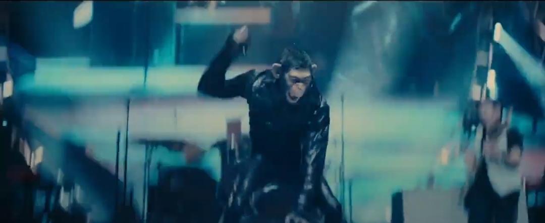 Anthropomorphic chimpanzee in a suit performing with a microphone on a concert stage before a crowd.