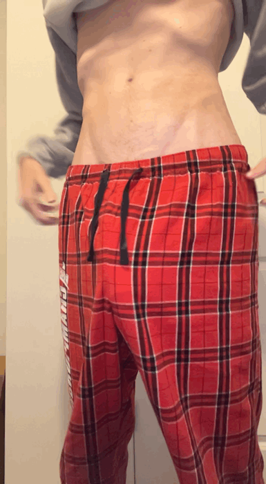 Slim white man in red plaid pajamas showing his big uncut cock in a bedroom selfie
