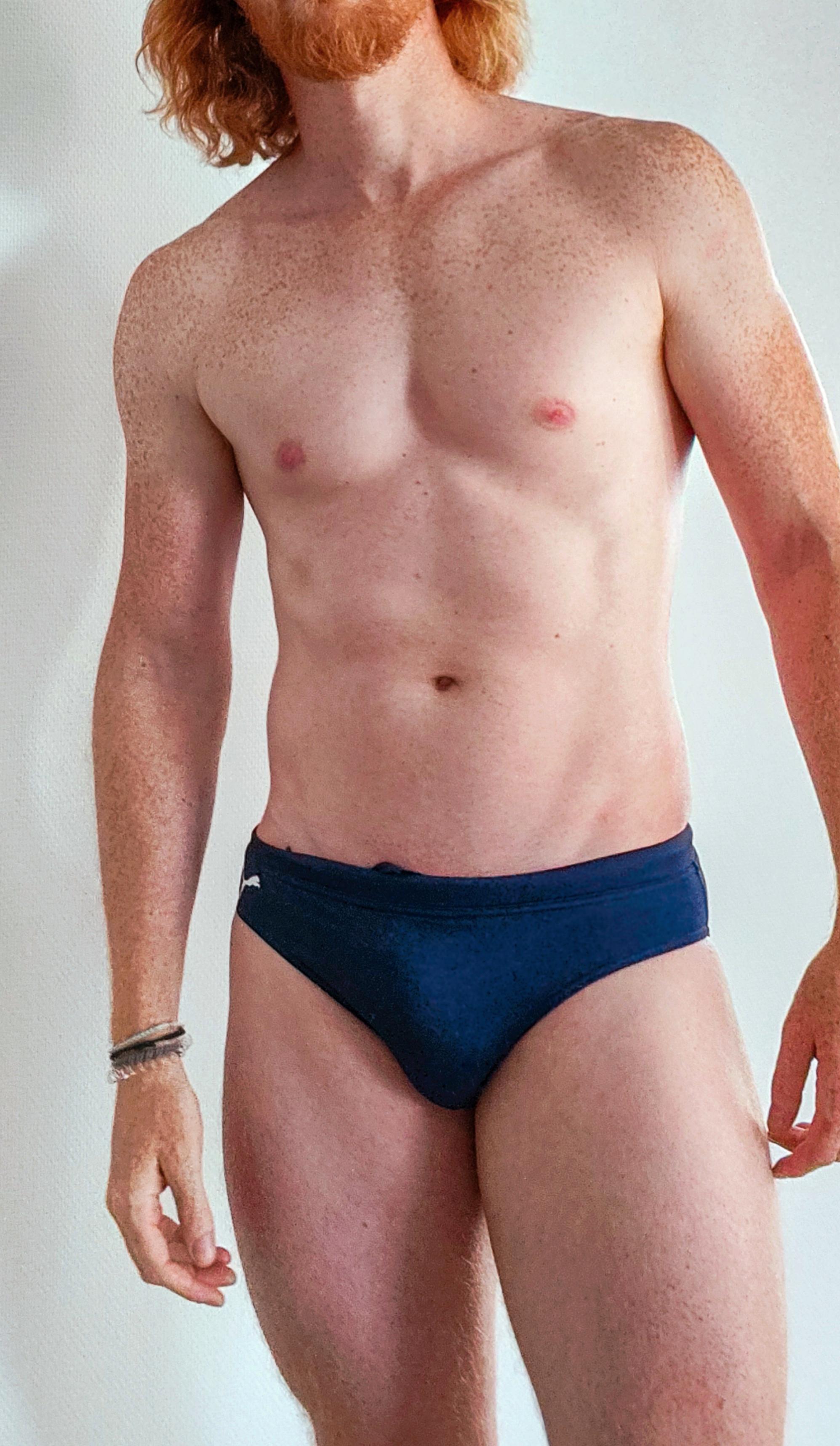 Athletic redhead man with freckles posing in blue speedos
