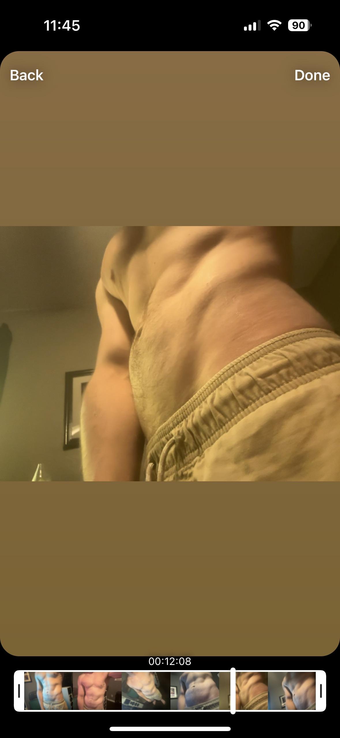 Muscular shirtless man in beige shorts posing for a fitness mirror selfie and a smartphone screen screenshot.