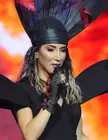 Yener wearing an elaborate black headpiece and dress while holding a microphone on stage