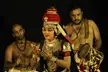 Kalamandalam Girija performing Koodiyattam with two musicians playing drums against a dark background
