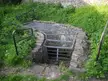 Entrance to the cellars in the Franconian Circle, featuring a metal grate over a stone-lined pit in green grass.