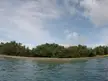 Cas Cay shoreline with green trees and a yellow kayak on the beach under a cloudy blue sky