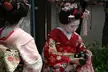 Two beautiful women in pink and red floral print kimonos with traditional updos and red lipstick.