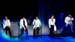 Big Bang kpop idols in white jackets and black pants performing on a dark stage with blue lighting and smoke