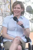 McKendry wearing a light blue short-sleeved shirt and khaki shorts, holding a microphone