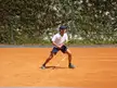 Tseng Chun-hsin in a white polo shirt and blue shorts playing tennis on a clay court