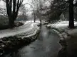 Roath Park in winter with a snowy landscape, a small stream, a path, and bare trees