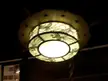 Close-up of a glowing ceiling lamp with intricate floral print patterns in a vintage tavern setting.