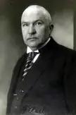 Friedrich Akel in a black and white vintage photo, wearing a dark suit and striped tie