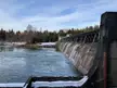 A concrete dam on the Lech river with water flowing over the spillway amidst a snowy winter forest.