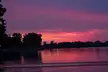 A river reflecting a vibrant purple and pink sunset sky with silhouettes of trees and a city skyline