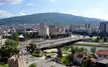 Skopje city skyline with a bridge over a river, urban buildings, and a large green mountain under a blue sky