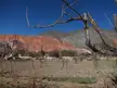 Cerro de Siete Colores landscape with red and grey mountains, a dry field, and a small village under a blue sky