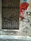 Vomit: a barred window with graffiti on the wall and shutters in an abandoned place