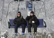 Putin and a companion in black ski gear and red sunglasses on a chairlift at a snowy mountain resort