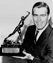 Pennel smiling in a dark suit and white shirt while holding the James E. Sullivan Award trophy