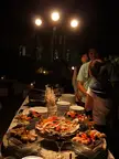 Petite Asian girls in white shirts and buns gathering around a sushi buffet at a resort night event.