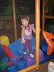 Girl with brown hair and pale skin in a purple outfit playing with foam blocks in a netted area