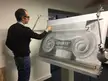 Francis Terry in a dark purple turtleneck drawing a black and white charcoal sketch of an ionic capital on an easel