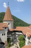 Bran Castle with red tiled roofs and a conical tower, featuring a couple in summer dresses in the courtyard
