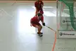 Two people in red athletic wear and short shorts playing floorball in a gym near a goal