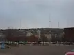 City skyline with a parking lot and tall radio towers on a hill under a cloudy sky