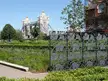 Tower Bridge in London viewed through a decorative metal fence and lush green gardens at Potters Field
