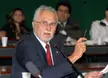 José Genoino in a pinstripe suit and glasses speaking into a microphone during a meeting in Brazil