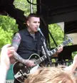 Nick 13 with extensive tattoos on his arms and neck playing electric guitar and singing on an outdoor stage.