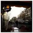 Cafe terrace view of a city street at dusk with a decorative light tree and pedestrians in winter clothing