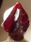 A close-up of a vermilion red crystal with sharp edges and a glossy, translucent surface.