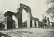 The iron pillar in Qutb Minar, featuring stone arches and pillars in a courtyard with two people in hats.
