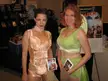 Booth babes in cosplay: a woman in a peach satin corset and hotpants and another in a green sparkling crop top and skirt.
