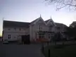 Large white wooden building with ornate gables, a silver car, and construction debris in a driveway.