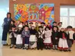Olentzeroren etorrera with children in traditional costumes, hats, vests, and white aprons by a painted backdrop