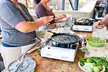 Two plus-size women in aprons preparing homemade bread and vegetables on a wooden table with portable stoves