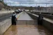 Two men in workwear and waders by concrete water channels at the Oroville Dam crisis site under a mesh canopy.