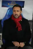 Pereira wearing a black coat and red scarf, sitting in a blue chair at a UEFA Europa League event