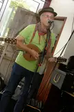 The Wassa Names wearing a hat and red and grey scarf playing a stringed instrument into a microphone