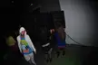 A group at a rave in a dark room with large speakers, featuring a man in a white hoodie and women in revealing clothing.