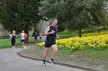 Six runners in athletic wear, tank tops, and short shorts running on a park path with yellow flowers and trees