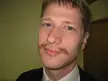 The Anti-Hitler, a man with light skin, blue eyes, and a thin brown mustache wearing a dark jacket and white shirt