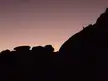Silhouette of a person on a rocky Joshua Tree mountain peak against a purple and orange sunset sky